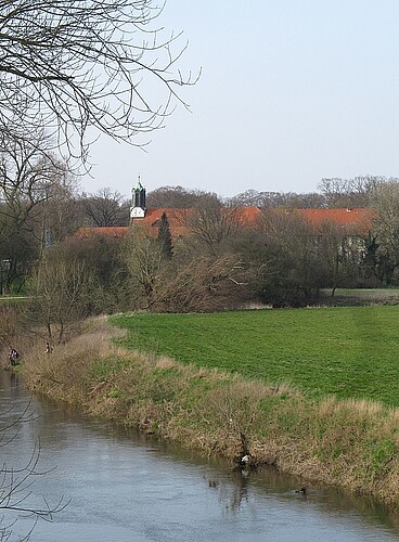 Das Kloster Marienwerder in Hannover von Ferne betrachtet mit einem Bachlauf im Vordergrund.