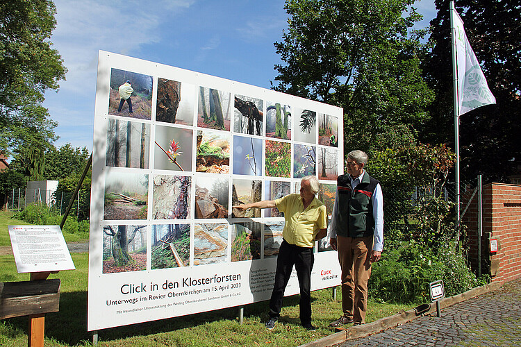 Zwei Männer stehen vor einer großformatigen Installation, die mit quadratischen Fotos bedruckt ist.