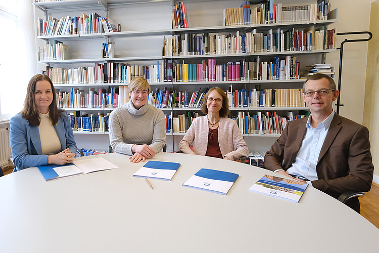Drei Frauen und ein Mann nebeneinander an einem runden Tisch vor einer Bücherwand