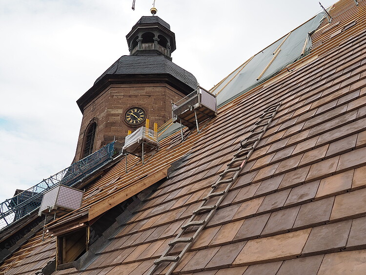 Kirchendach, teilweise gedeckt. Kirchturm. Baugerüst. Rötliche Dachplatten.