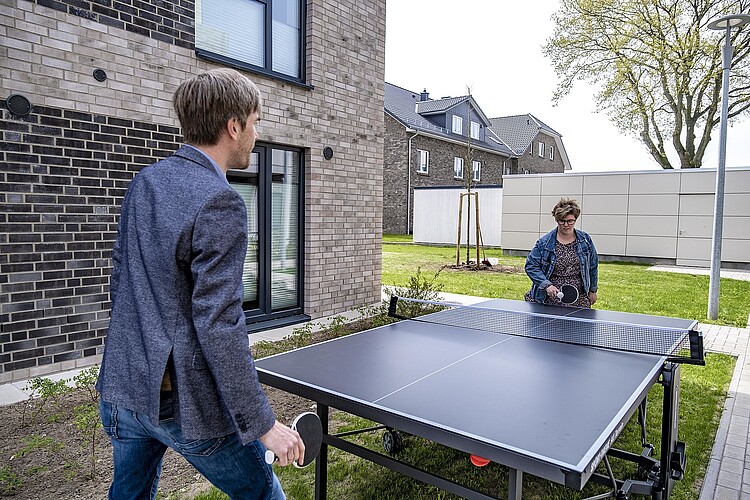 Ein Mann und eine Frau spielen in einem Garten Tischtennis.