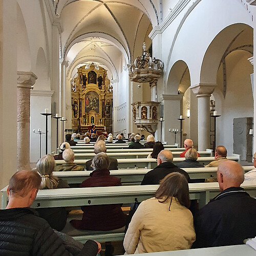 Viele Menschen sitzen auf Bänken in der Kirche, vorne wird Musik gespielt.