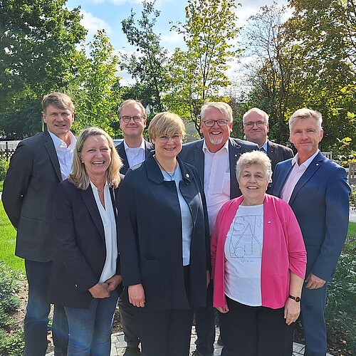 Gruppenbild mit fünf Männern und drei Frauen in einem Park bei Sonnenschein