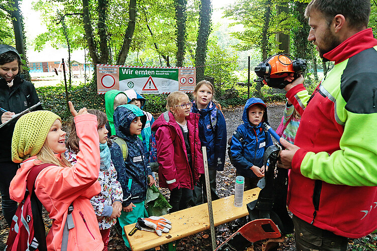 Ein Forstwirt der Klosterforsten zeigt einer Gruppe von Grundschülern im Wald, welche Schutzkleidung er benötigt.
