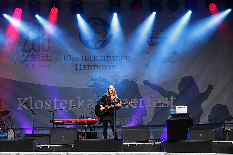 eine Frau steht mit einer Gitarre auf der Bühne und singt.
